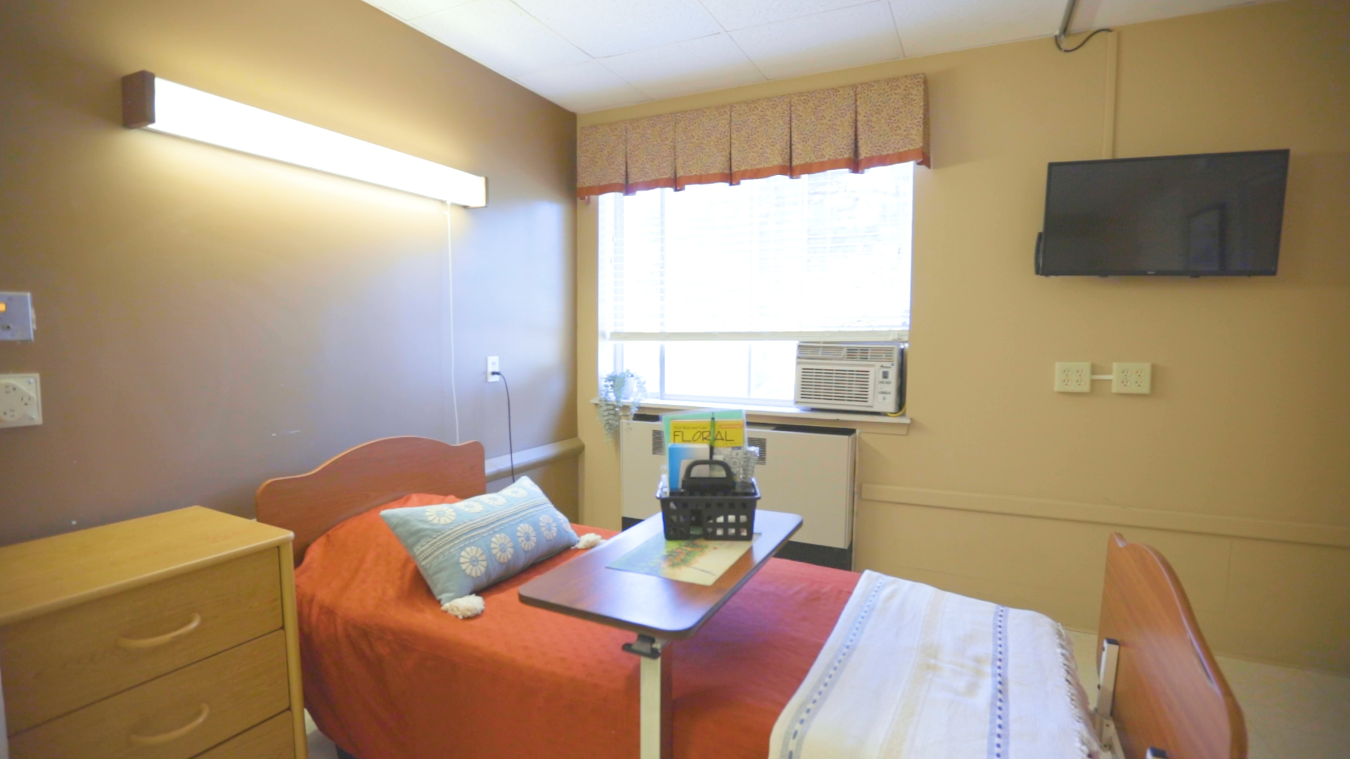 Room with one bed and bed table and television on the wall.